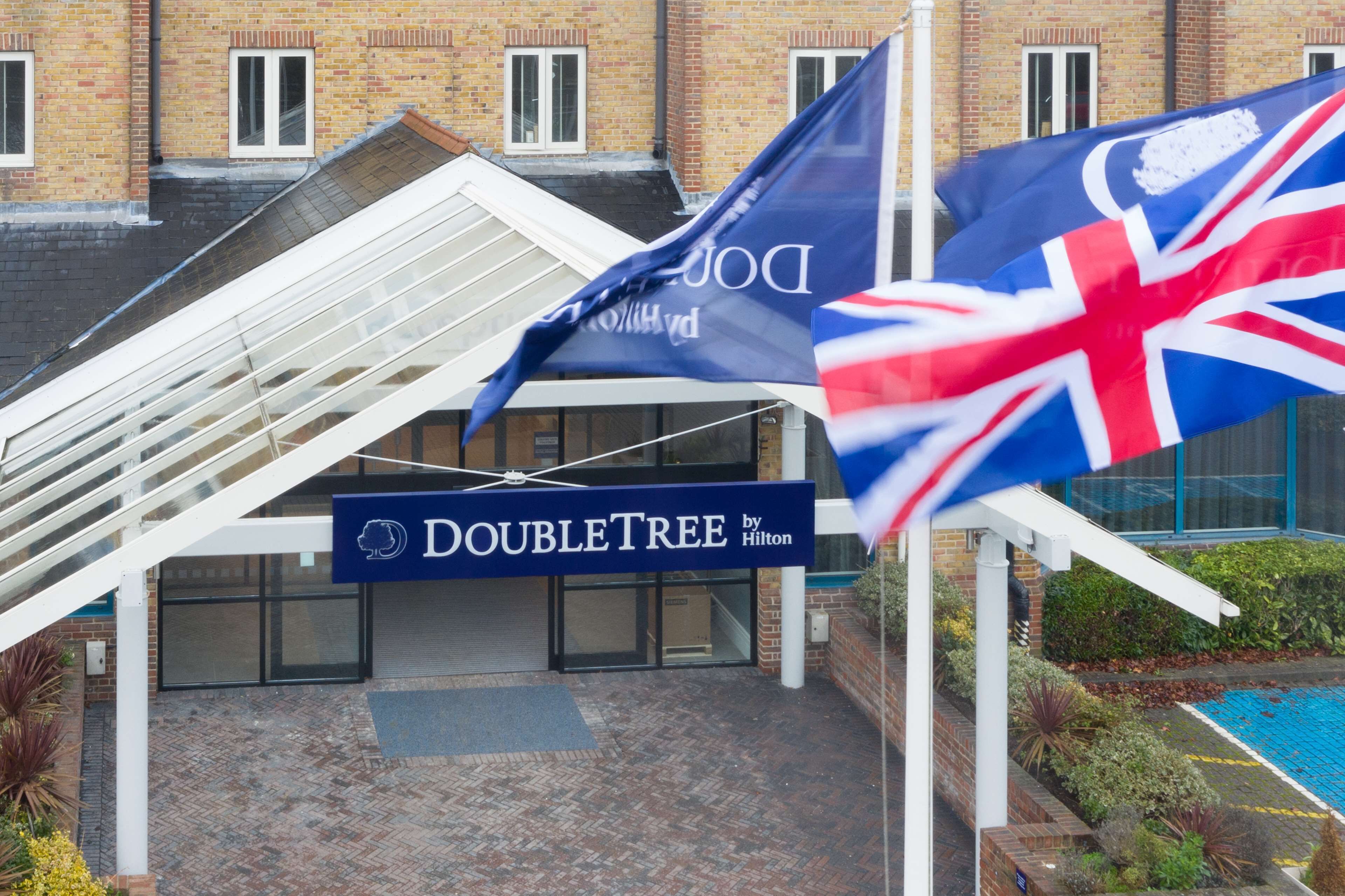 L’entrée d’un hôtel DoubleTree by Hilton, avec un auvent en verre, une piscine et des drapeaux.