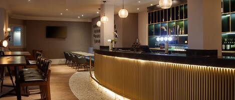 A bar area with a curved counter, pendant lighting, and a seating arrangement with tables and chairs.