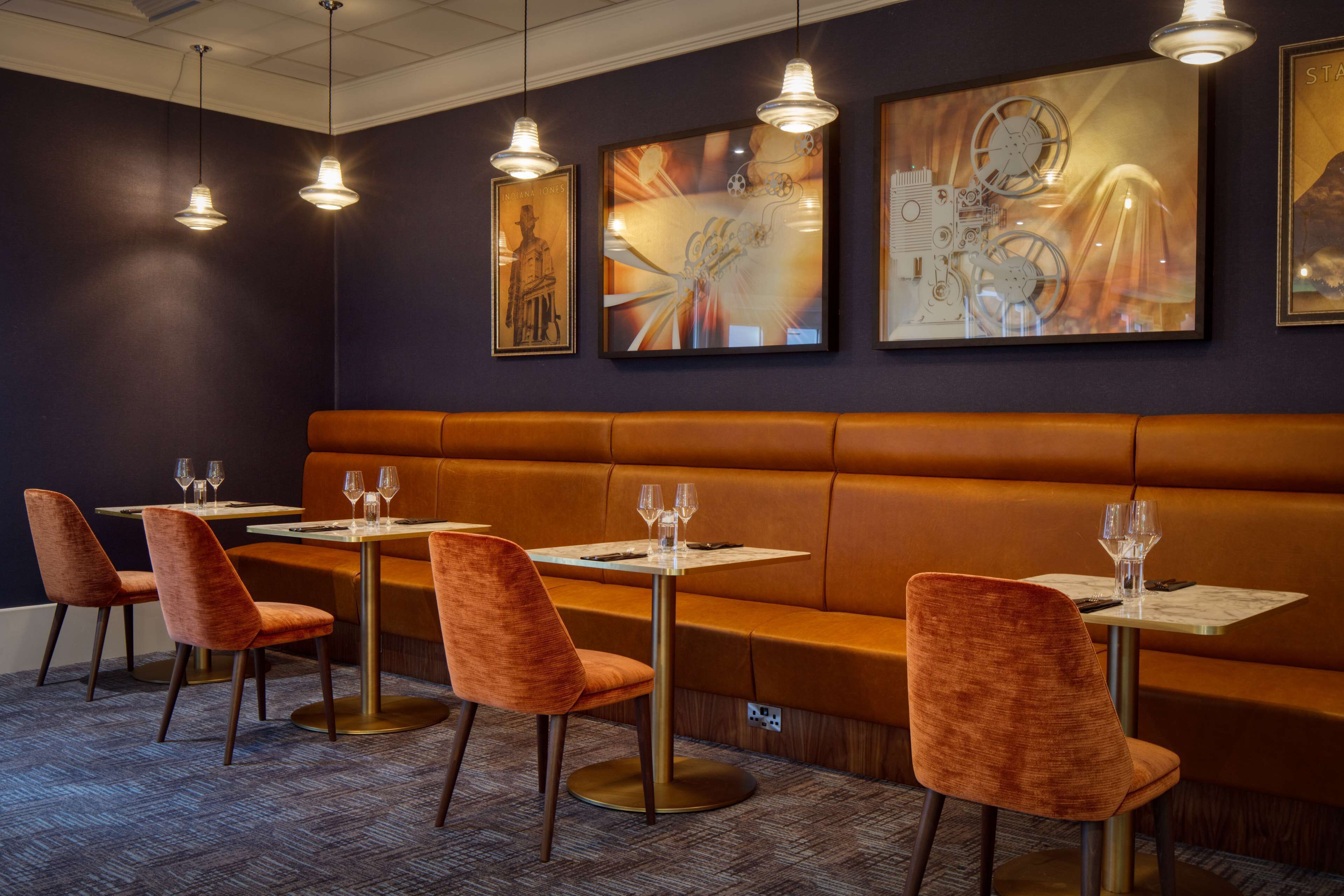 A restaurant with a dark wall, orange seating, and framed artwork.