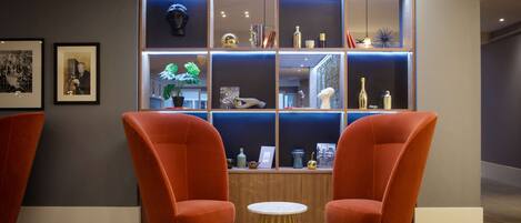 A modern interior with two orange armchairs, a small round table, and a wall-mounted display case with various items.