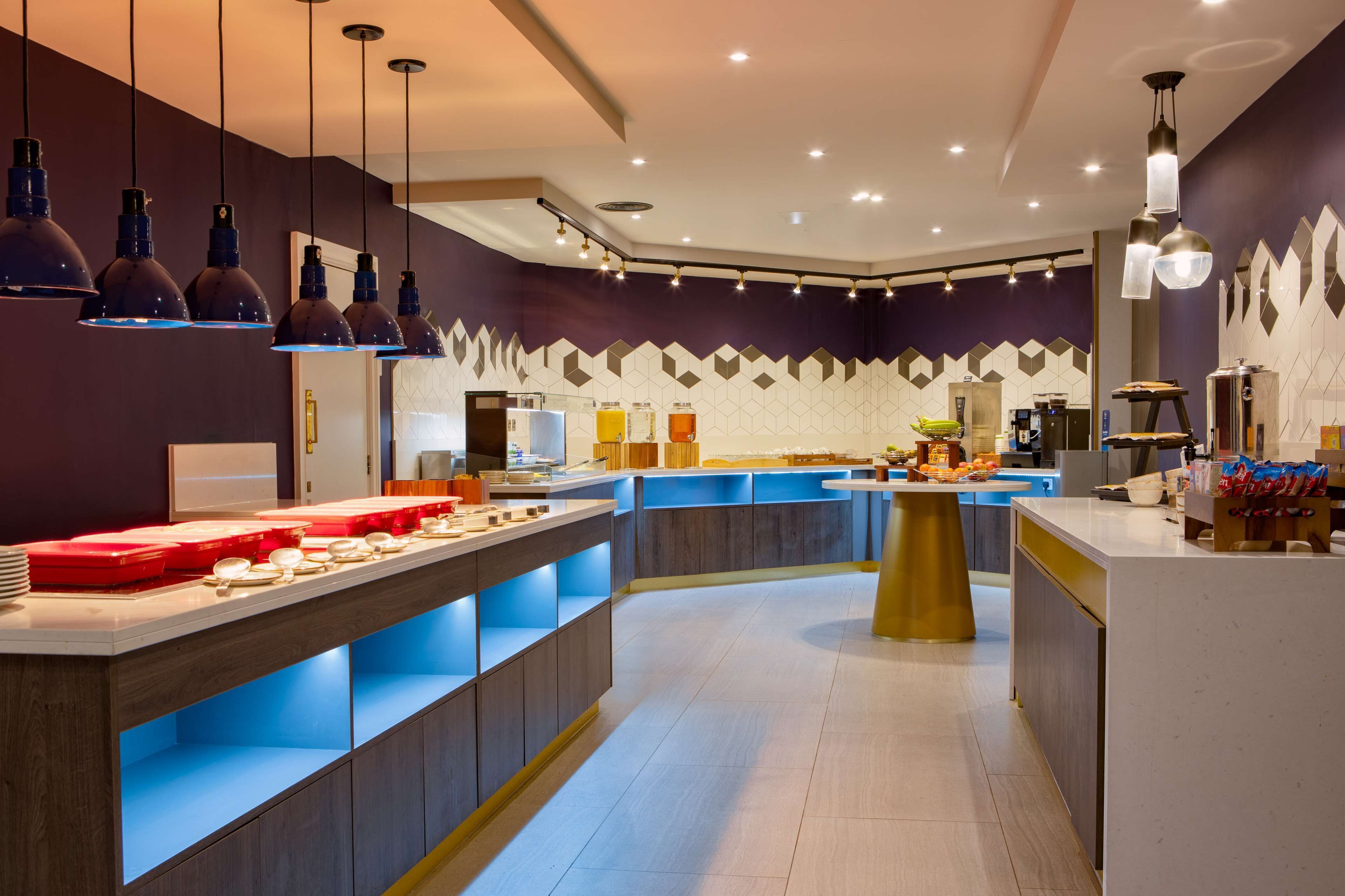 Une cuisine moderne dotée d’un îlot central, d’étagères bleues rétroéclairées et de luminaires suspendus.