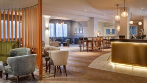 A modern hotel lobby with a curved seating area, a reception desk, and a dining area. - DoubleTree by Hilton London Elstree (Borehamwood)