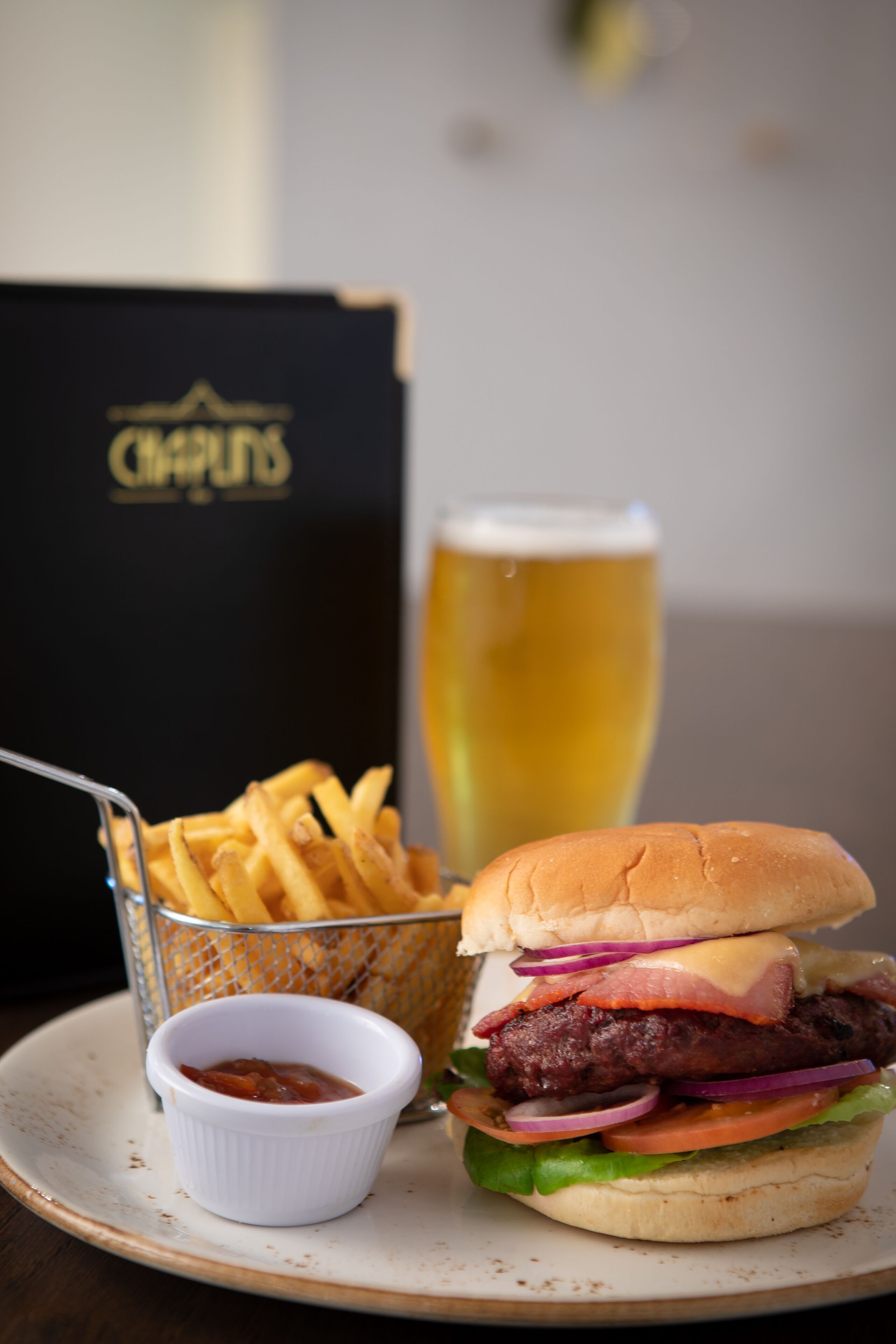 A burger with fries and a beer on a plate.