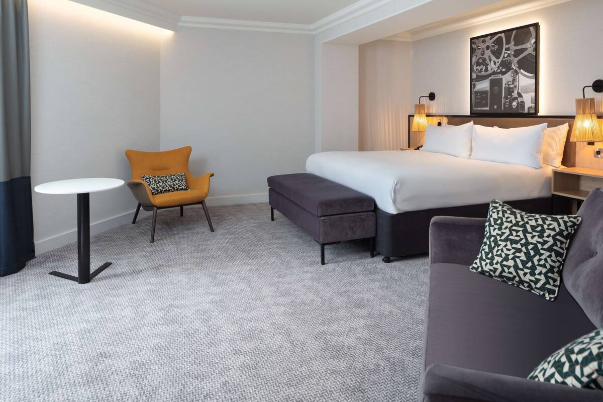 A hotel room with a bed, a sofa, a small table, and a chair.