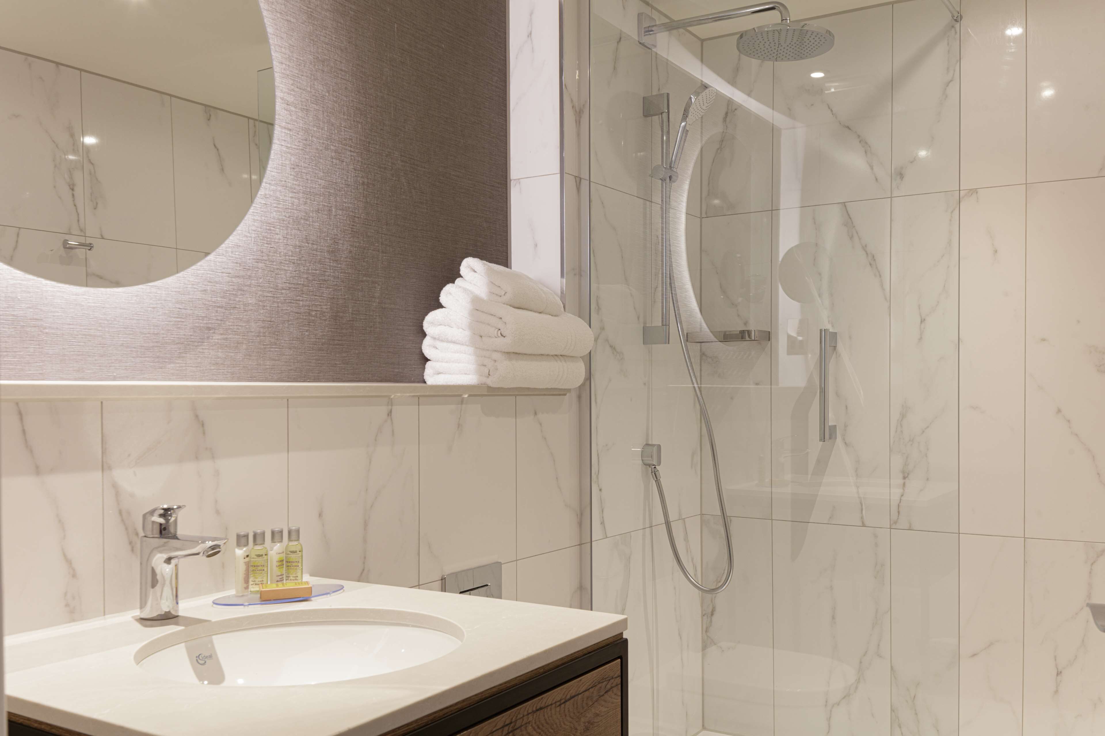 A modern bathroom with a marble sink, a large mirror, and a glass-enclosed shower area.