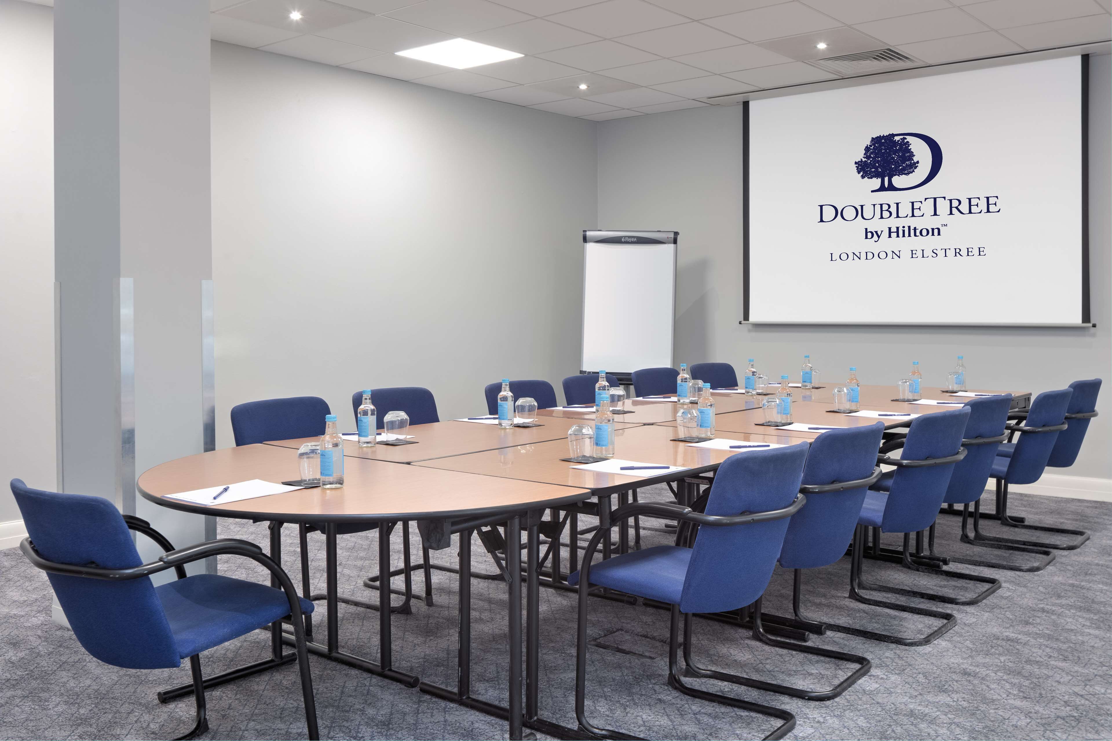 Une salle de conférence équipée d’une grande table, de chaises bleues, de bouteilles d’eau et d’un écran de présentation affichant le logo de DoubleTree by Hilton.