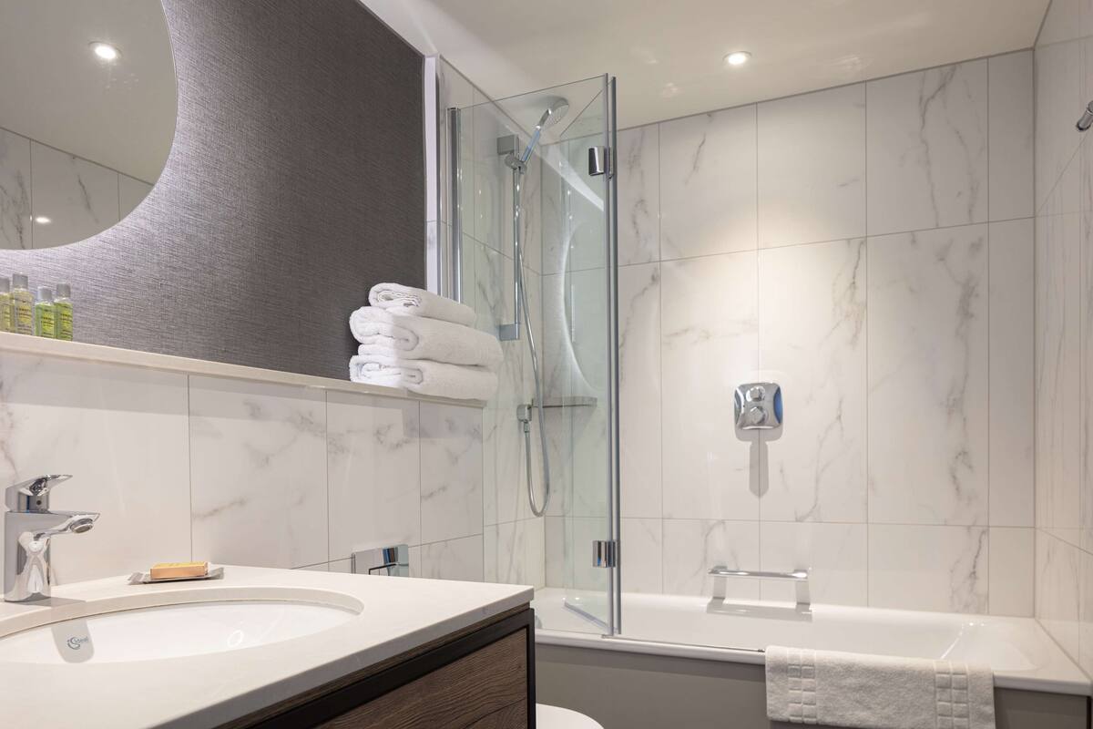 A modern bathroom with a glass-enclosed shower, a large mirror, and a marble-tiled wall.