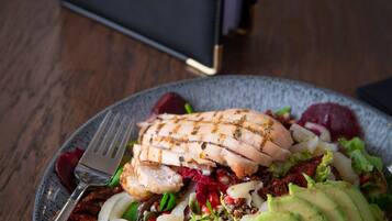 A plate of food with grilled chicken, avocado, and greens on a table with a dark blue menu in the background.