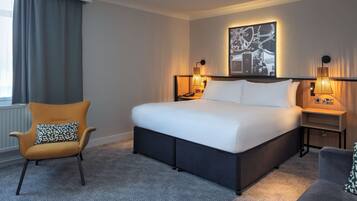 Una habitación de hotel con una cama grande, una silla, una mesita de noche y una lámpara de pared.