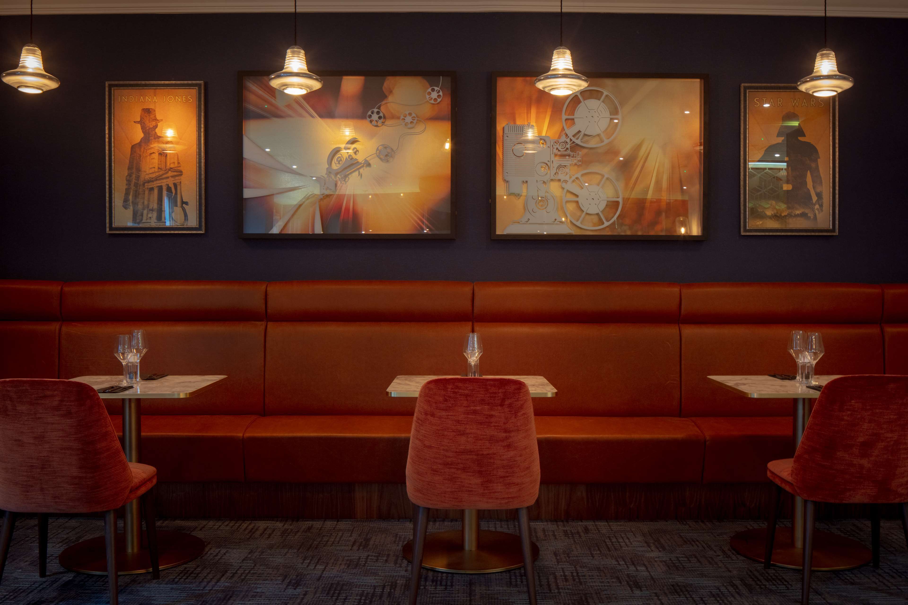 Un restaurante con un largo banco naranja, sillas rojas y cuadros en la pared.