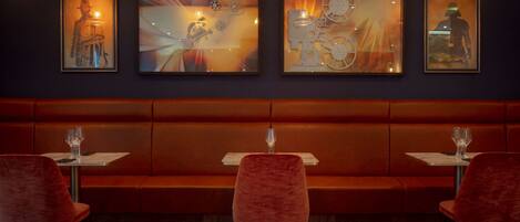 Un restaurante con un largo banco naranja, sillas rojas y cuadros en la pared.