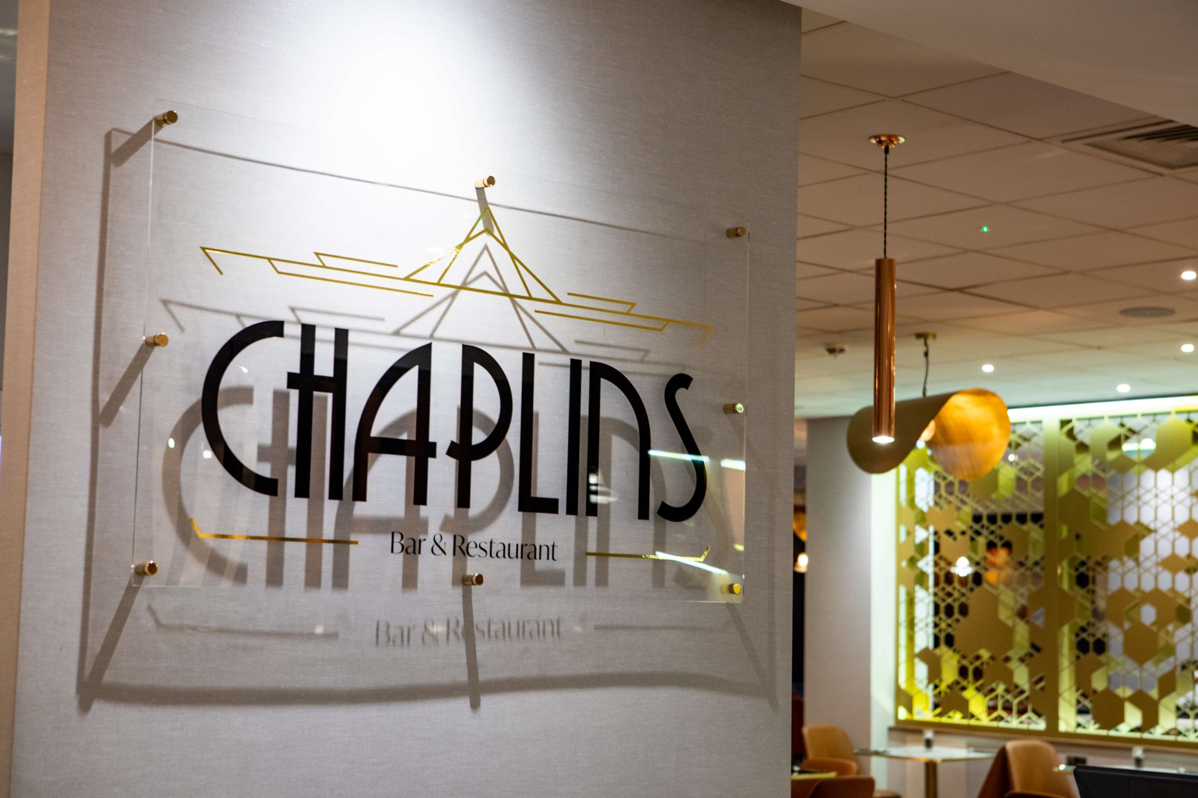 A sign for 'CHAPLINS Bar & Restaurant' with a geometric design and hanging elements.
