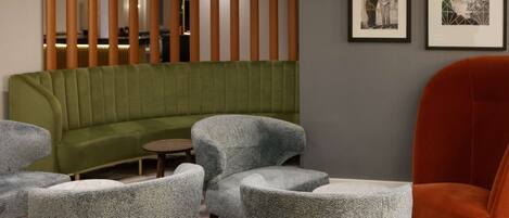 A modern lounge area with a green sofa, grey armchairs, and a red chair. There are framed pictures on the wall.