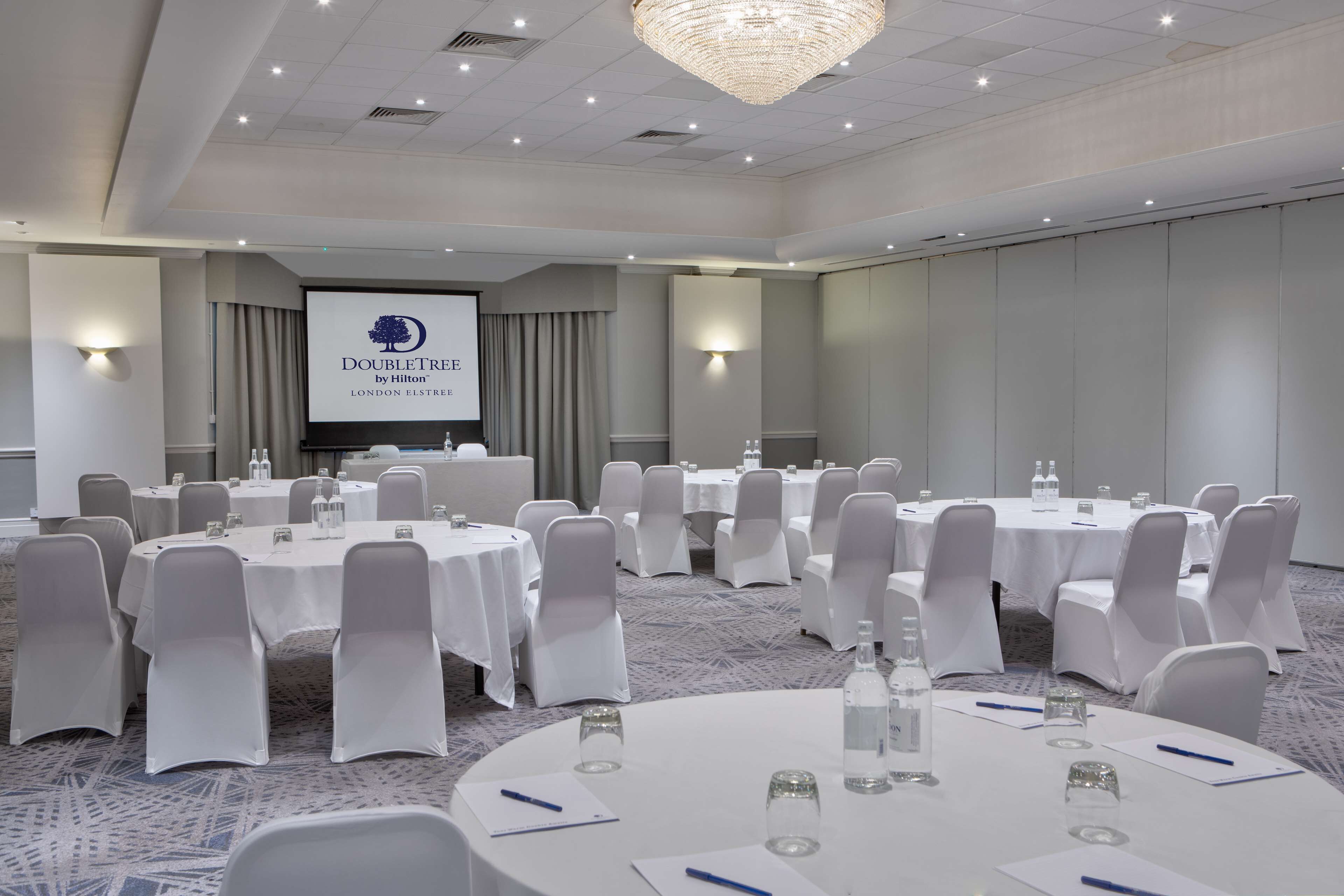 A conference room with round tables, white chairs, and a large screen displaying the DoubleTree by Hilton logo.