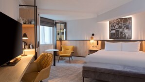 A hotel room with a bed, a desk with a lamp, a chair, a TV, and a large painting on the wall. - DoubleTree by Hilton London Elstree (Borehamwood)