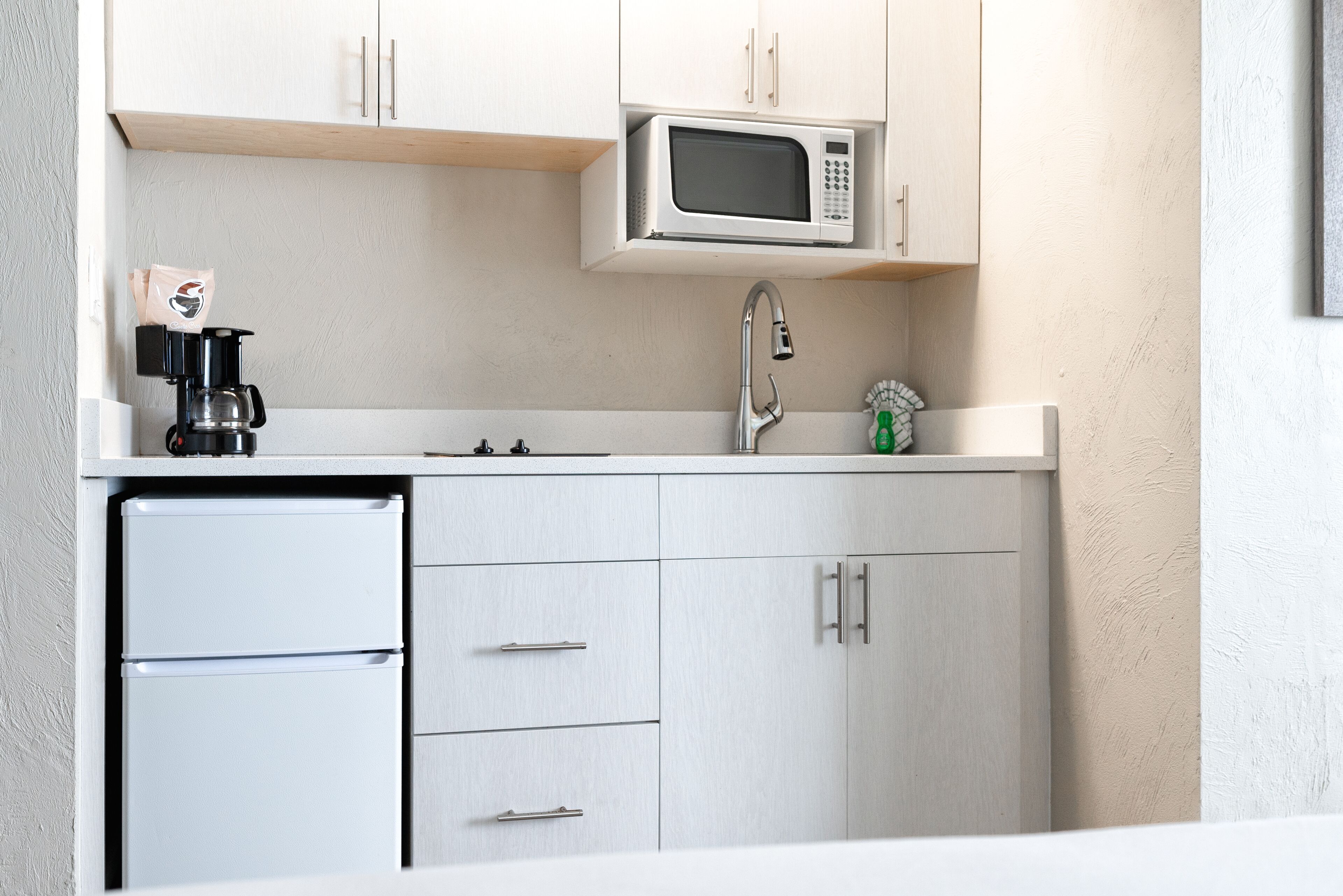 A compact kitchen with a microwave, coffee maker, and a small refrigerator.