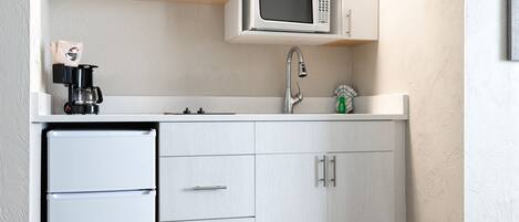 Una cocina compacta con microondas, cafetera y refrigerador pequeño.