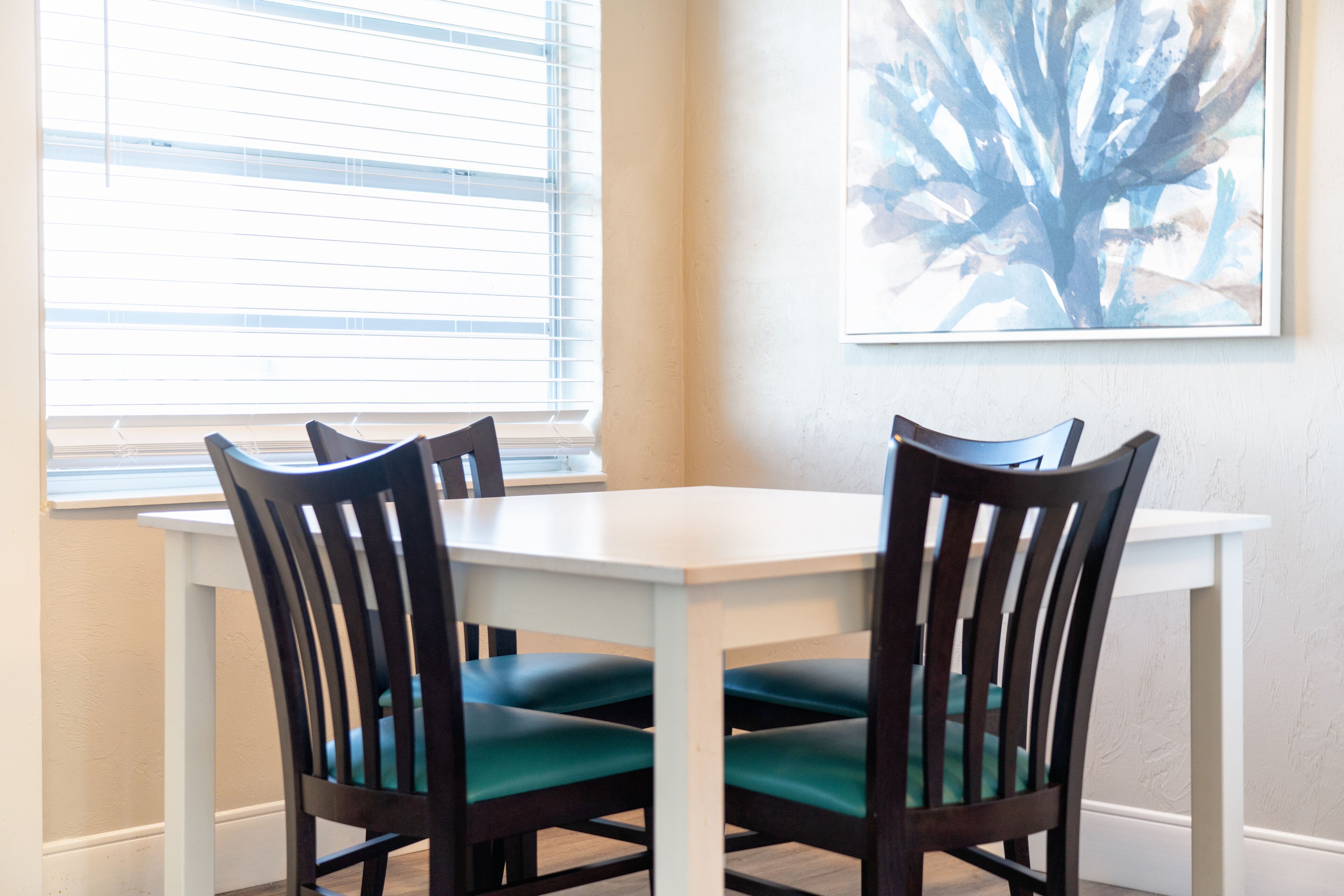 Un comedor con una mesa blanca y cuatro sillas de madera oscura con cojines verdes.