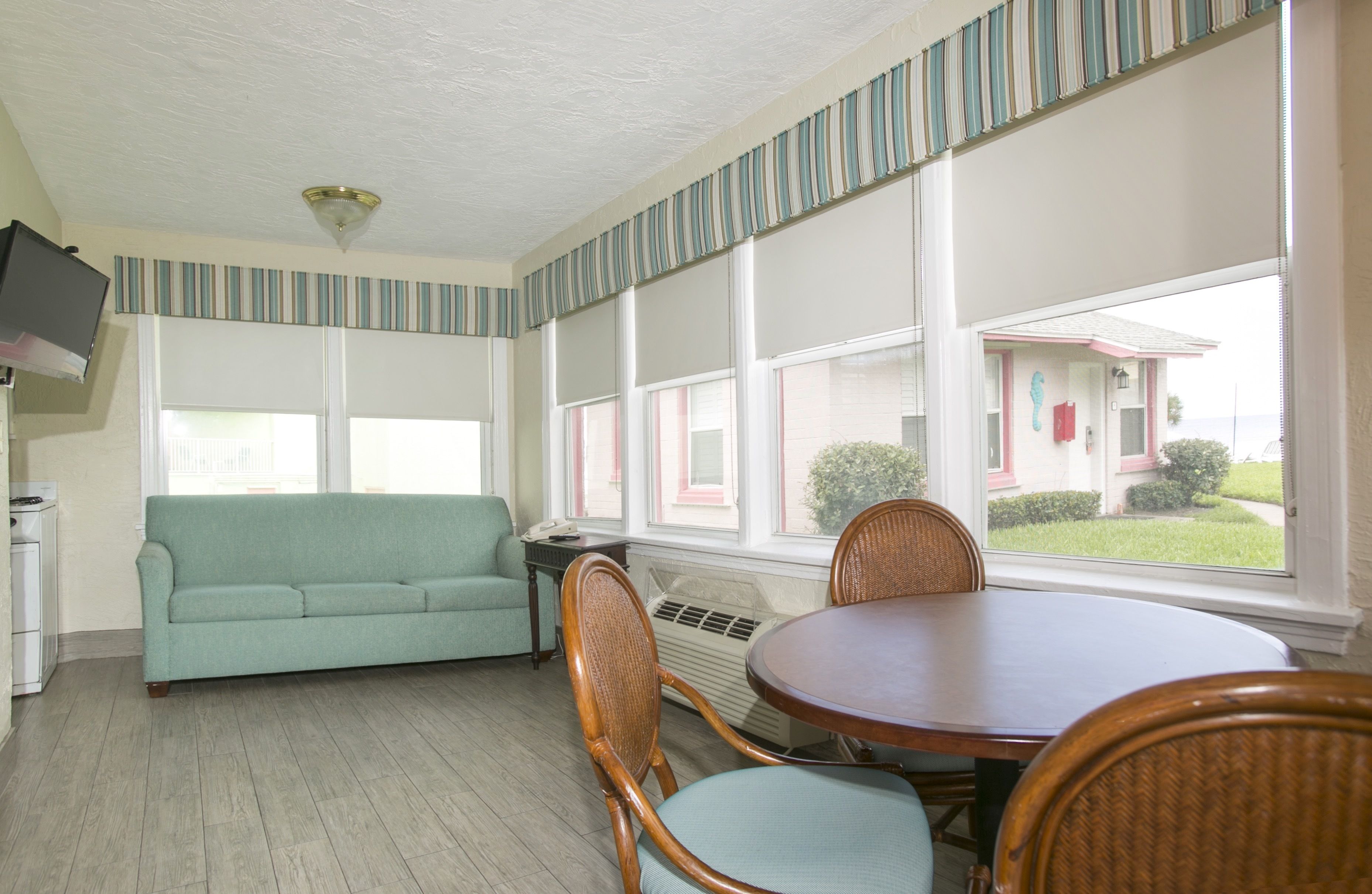 A room with a sofa, chairs, a table, and large windows.