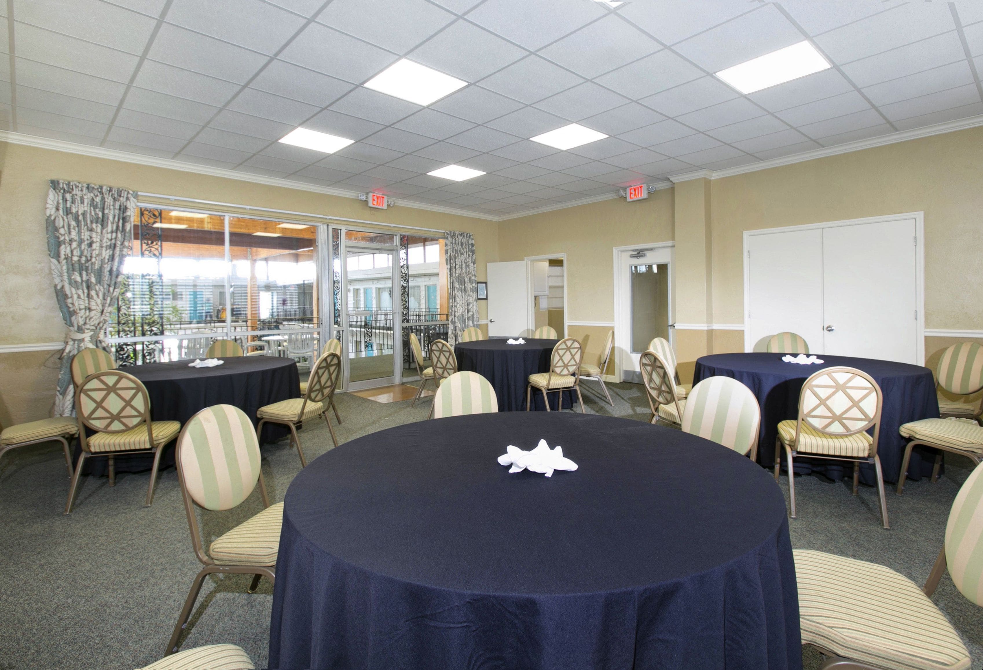 A conference room with round tables, chairs, and a view through a glass door.