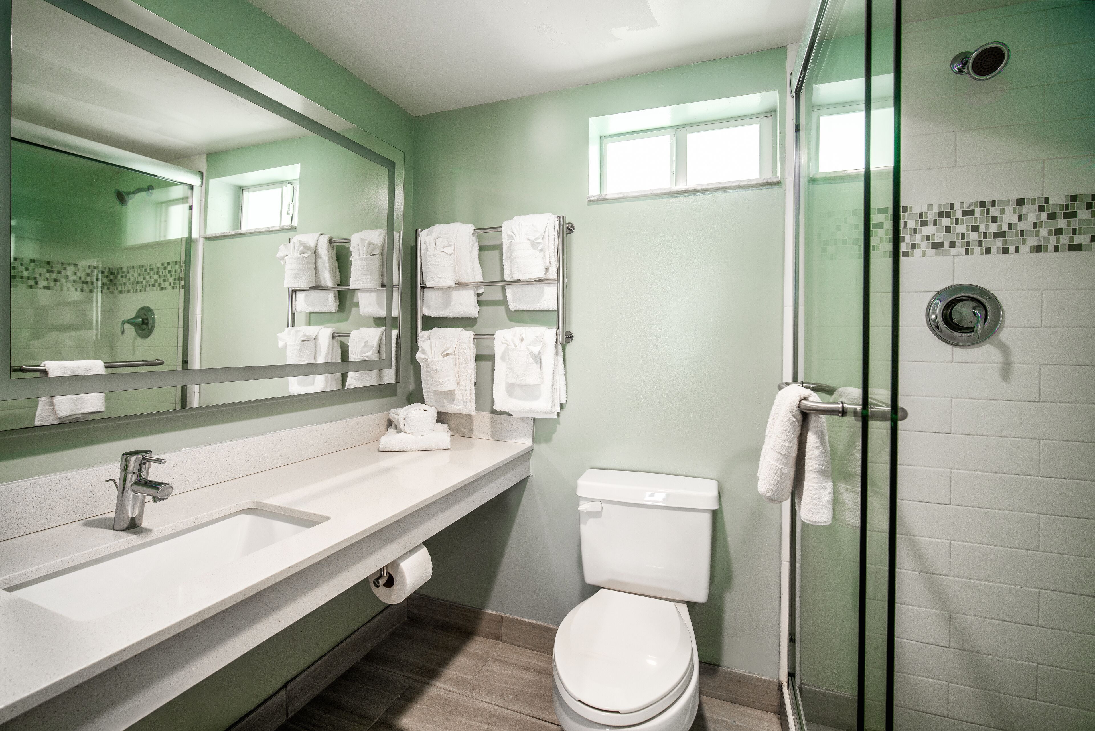 A bathroom with a white sink, mirror, and toilet, glass shower enclosure, and a towel rack with multiple towels.