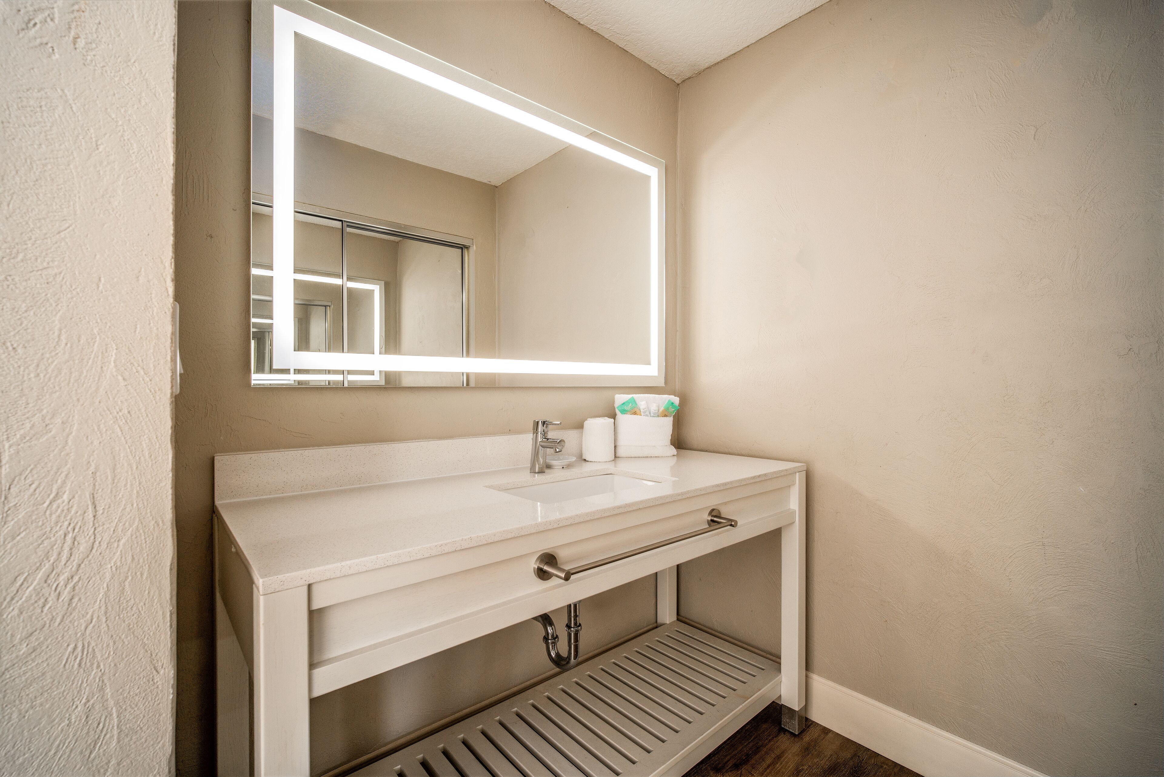 A bathroom with a white vanity, a mirror with LED lighting, a towel rack, and a toilet paper holder.