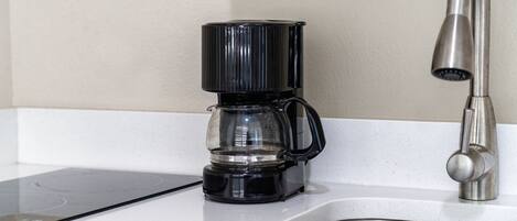 A kitchen with a coffee maker on the counter and a stainless steel sink.