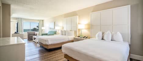 A hotel room with two beds, a desk, a chair, and a view of the ocean.