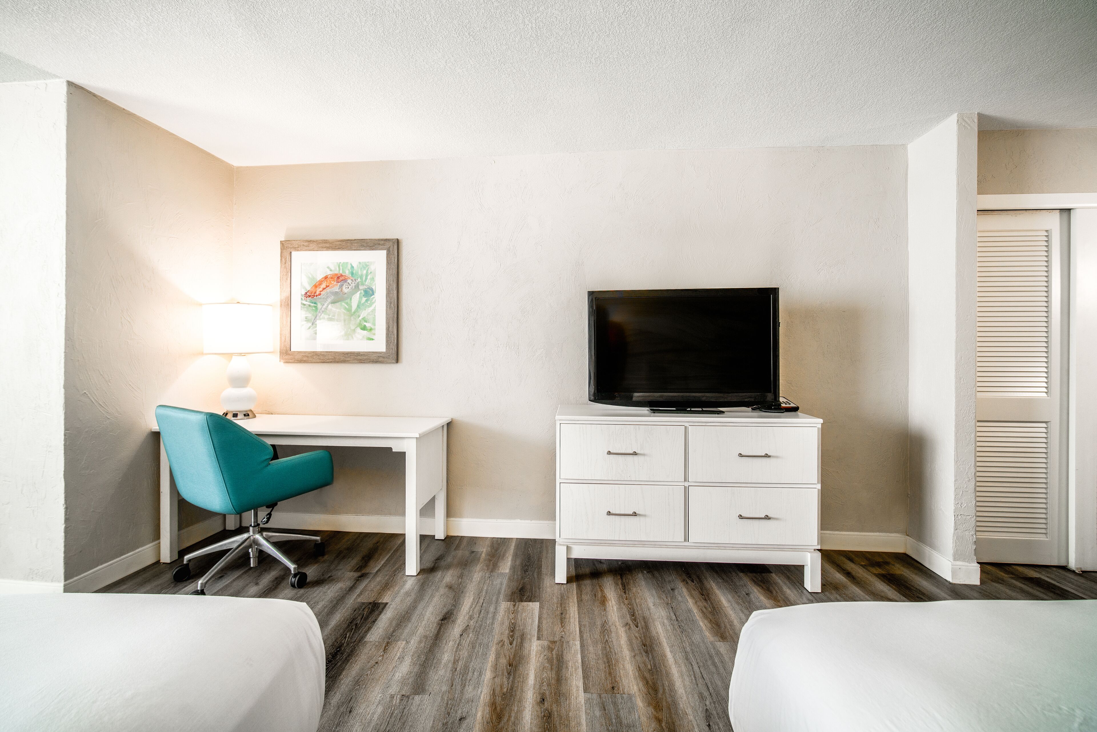 A hotel room with a desk, a television, and two beds.