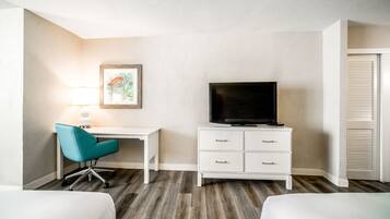 A hotel room with a desk, a television, and two beds.