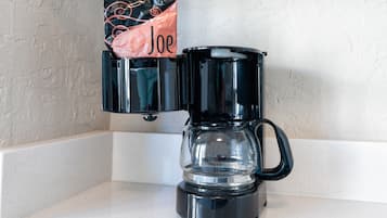 A black coffee maker with a clear carafe and a bag labeled "Joe" on the counter.