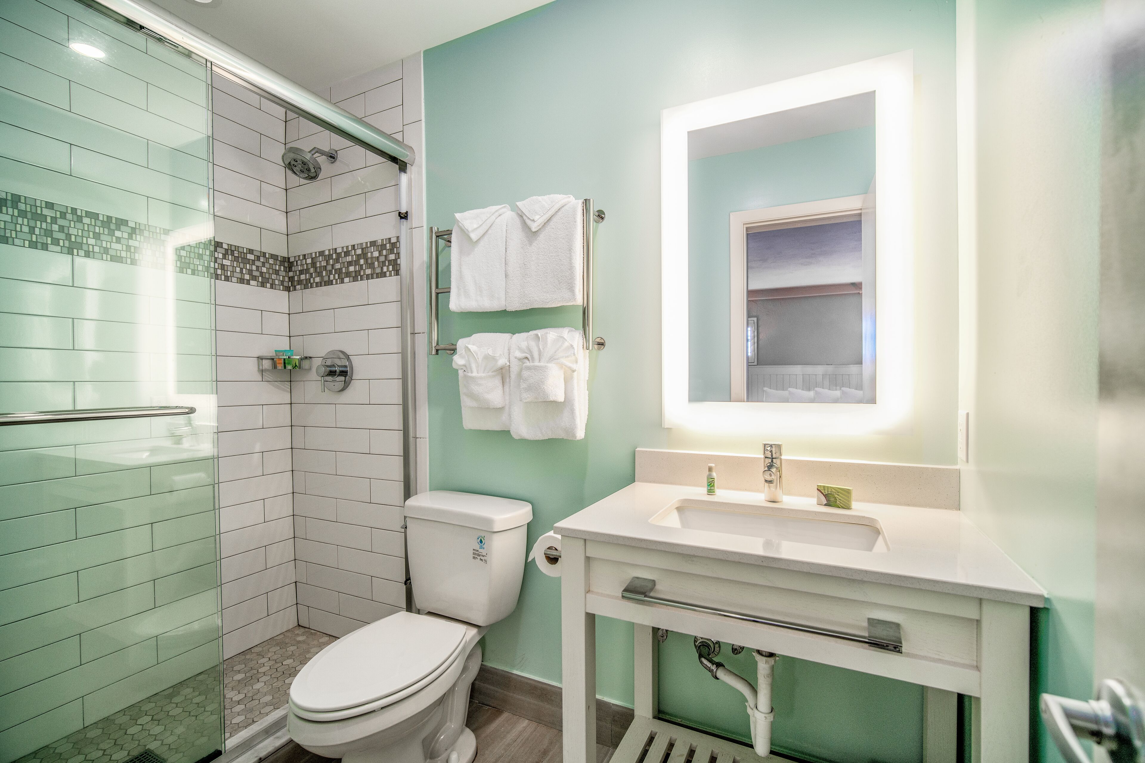 A bathroom with a glass shower enclosure, a toilet, a sink with a mirror, and towels hanging on a rack.