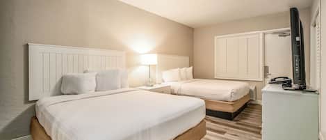 Une chambre d’hôtel avec deux lits, une table de chevet avec une lampe, une commode et un téléviseur.