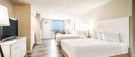 A hotel room with two beds, a TV, a desk, and a balcony with a view.