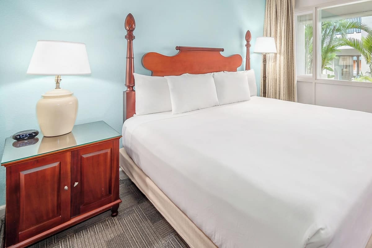 A neatly made bed with white linens, a wooden headboard, and two bedside lamps.