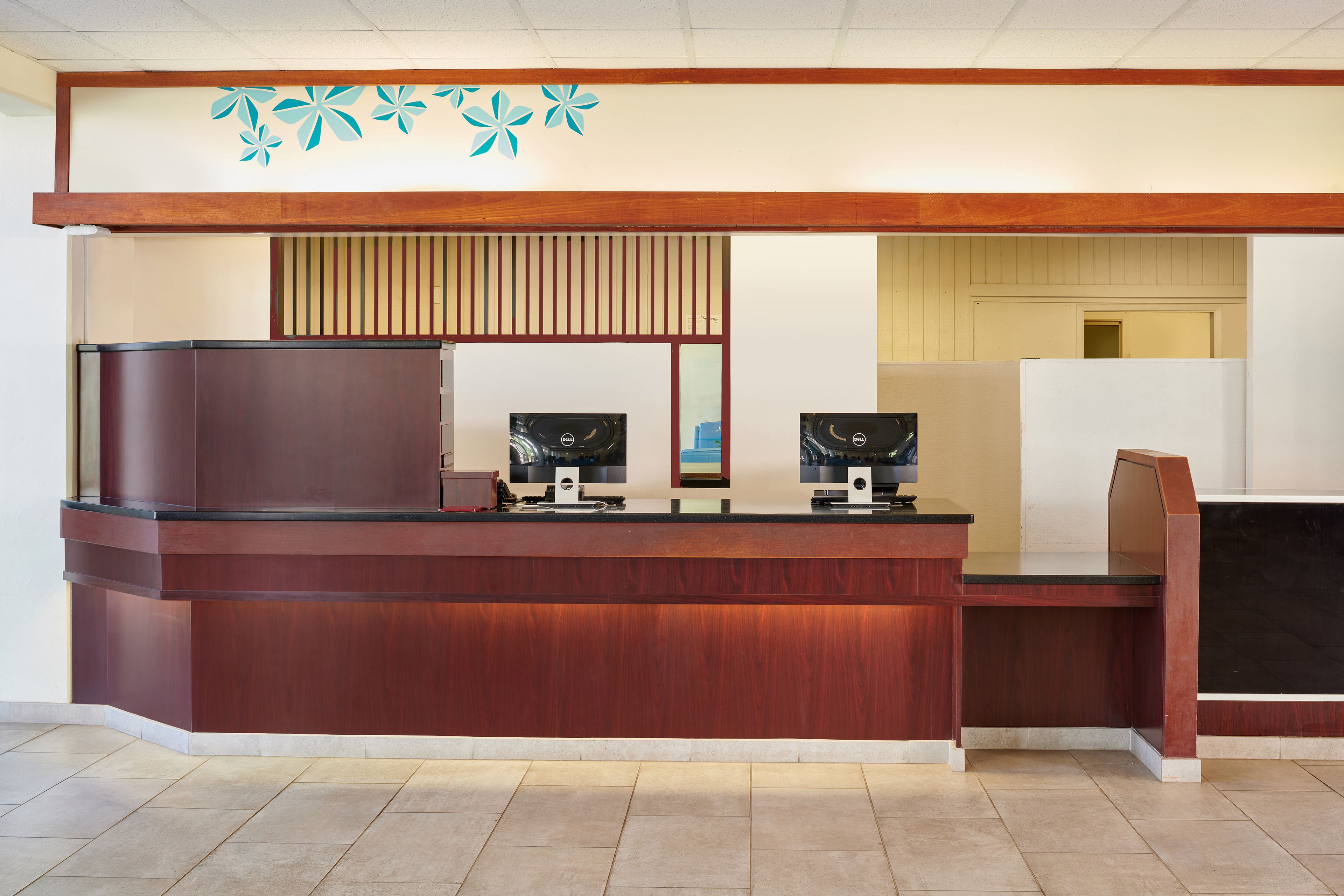 A reception desk with two monitors, a wooden counter, and a decorative wall with a floral pattern.