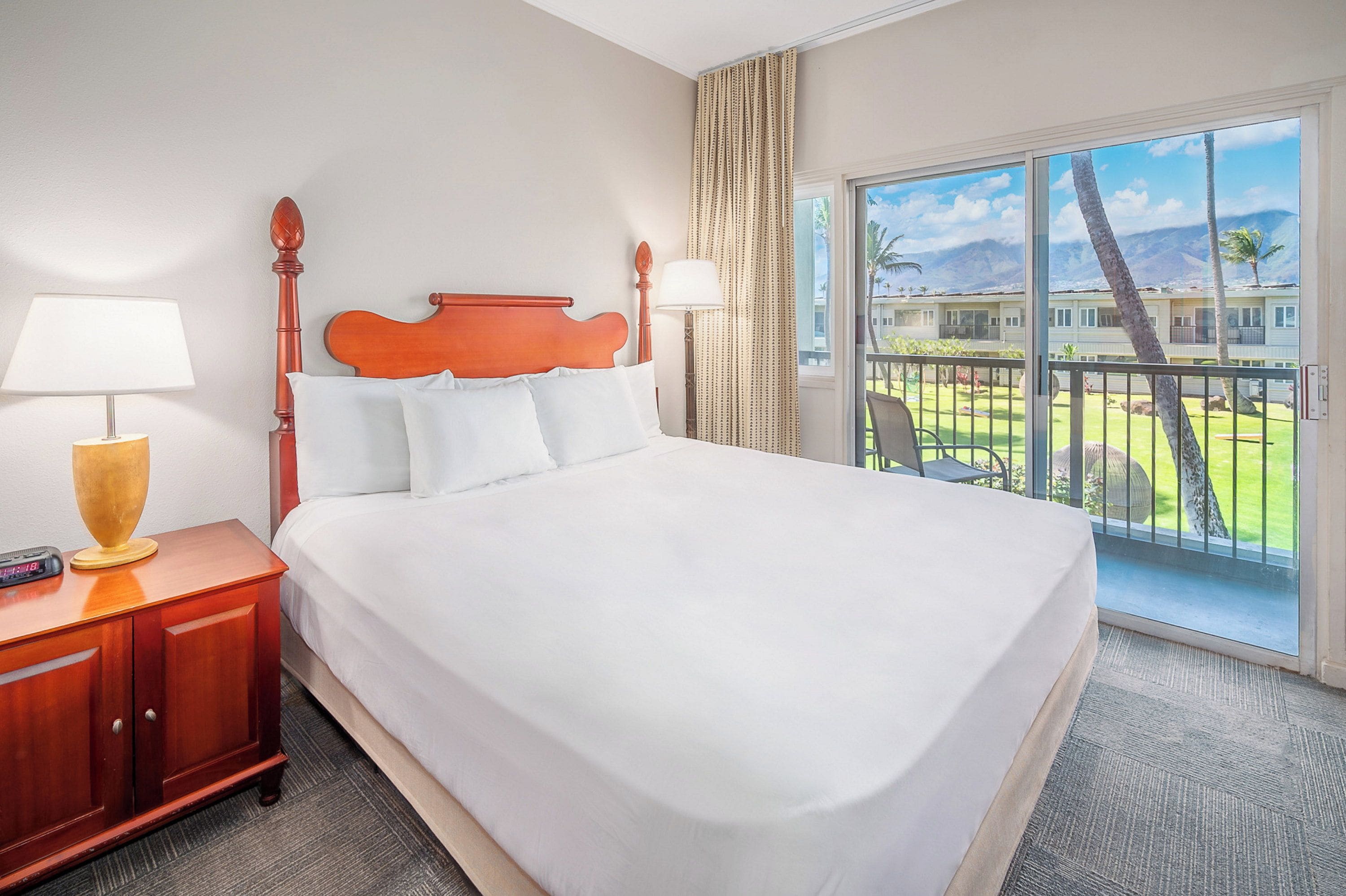 A hotel room with a large bed, a nightstand, a lamp, and a view of a resort area.