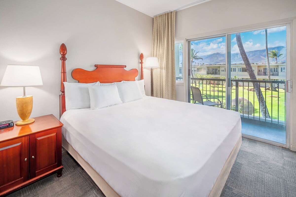Una habitación de hotel con una cama grande, una mesita de noche, una lámpara y vistas a una zona turística.