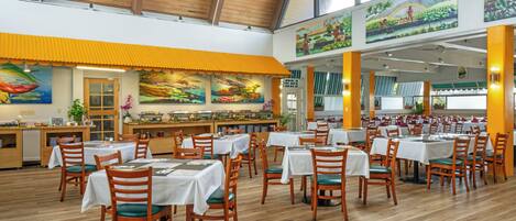 A spacious restaurant with high ceilings and wooden beams, featuring multiple dining tables and chairs, and artwork on the walls.