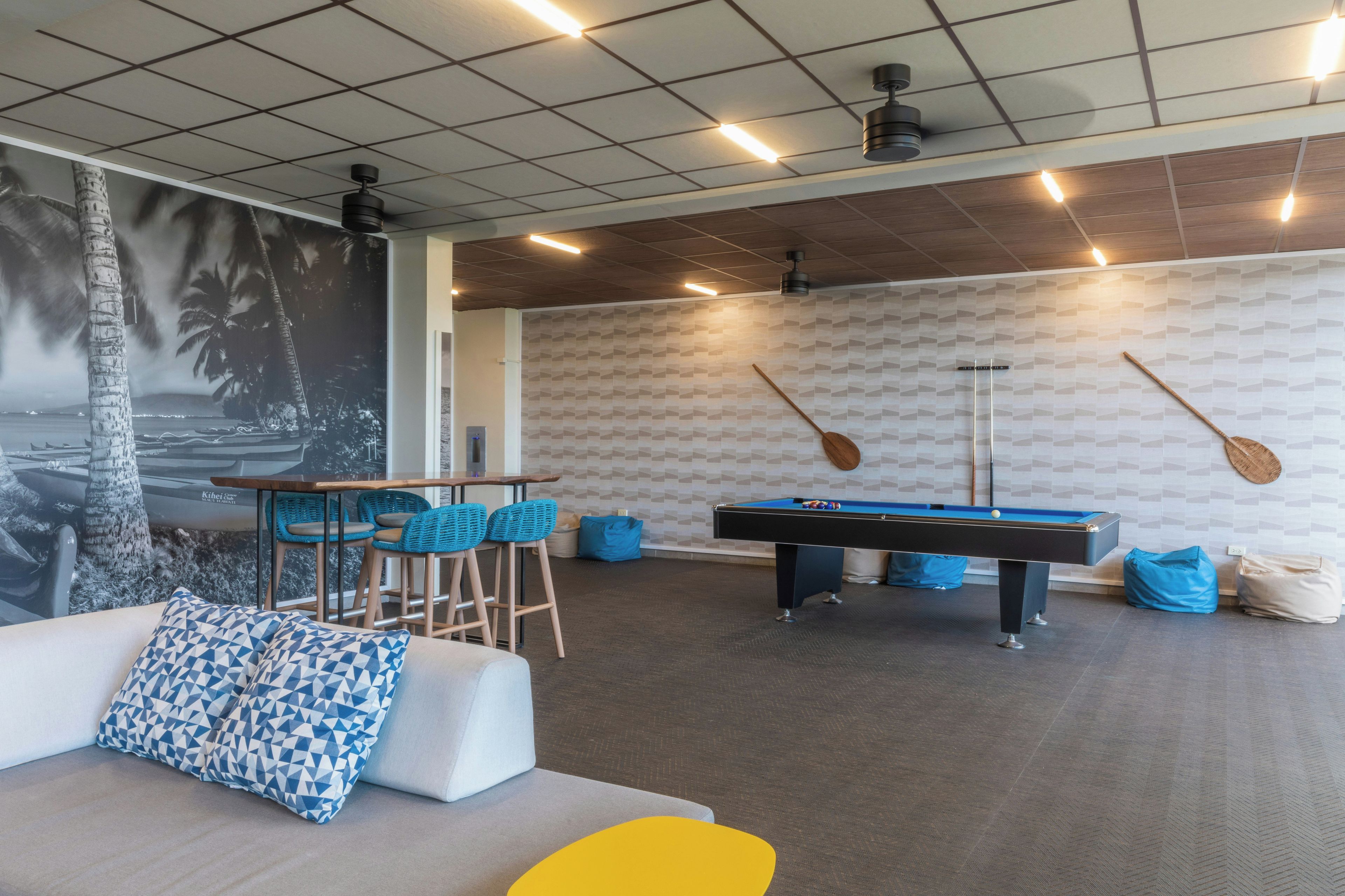 A pool table in a room with a geometric patterned wall, a sofa with patterned cushions, and a mural of palm trees.
