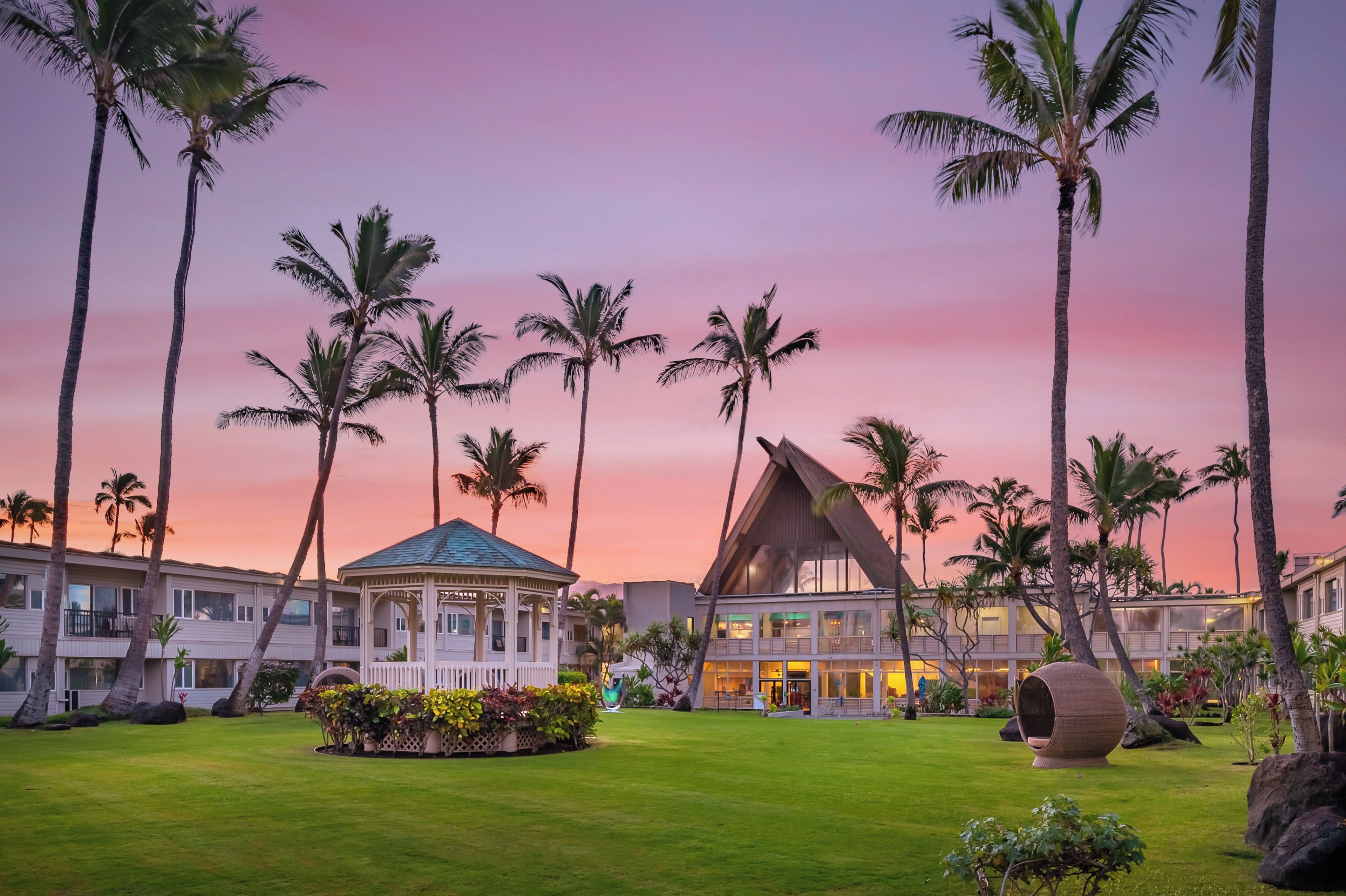 A resort with a central building, palm trees, and a well-maintained lawn.