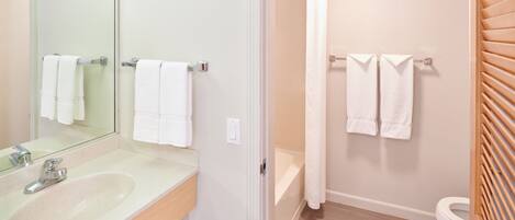 Une salle de bain équipée d’un lavabo, d’un miroir, d’un porte-serviettes, d’un rideau de douche et de toilettes.
