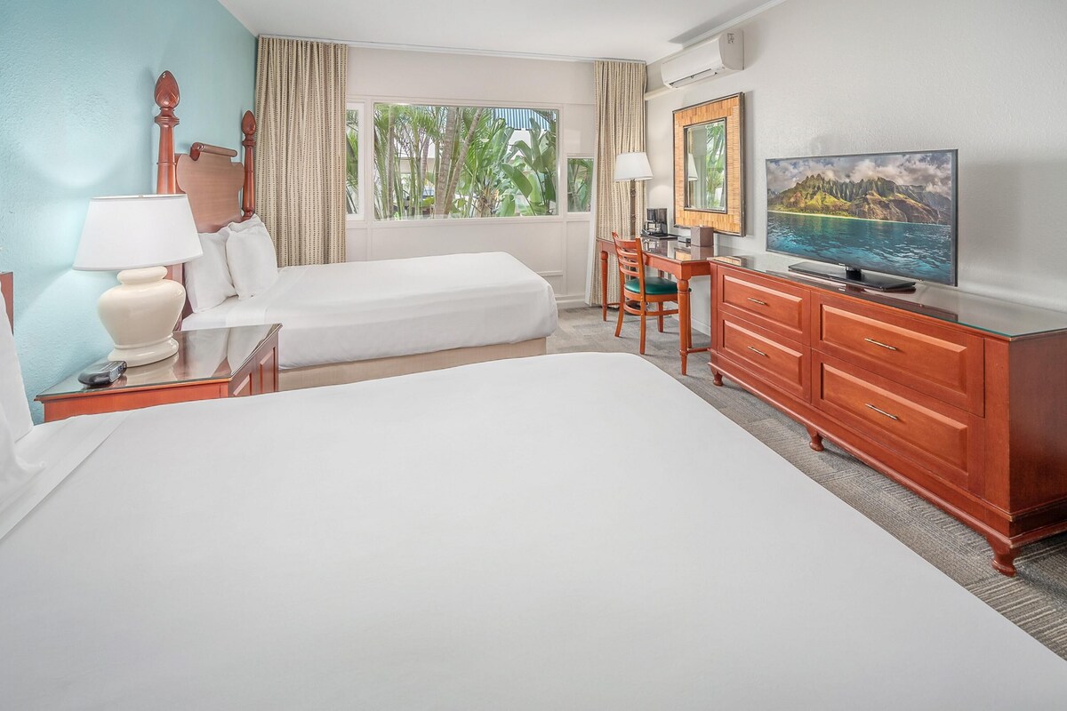 A hotel room with a bed, a desk, a television, and a window with a view of greenery.