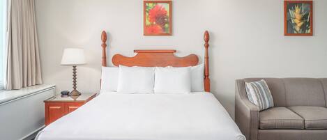 Una habitación de hotel con una cama grande, una mesita de noche con lámpara, un sofá y dos cuadros colgados en la pared.