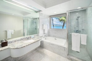 A modern bathroom with a large mirror, a bathtub, a shower, and a view of the ocean. - Maui Beach Hotel (Kahului)