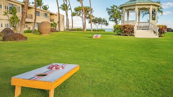 A well-maintained lawn with a picnic table, a gazebo, and a building with a pool in the background.
