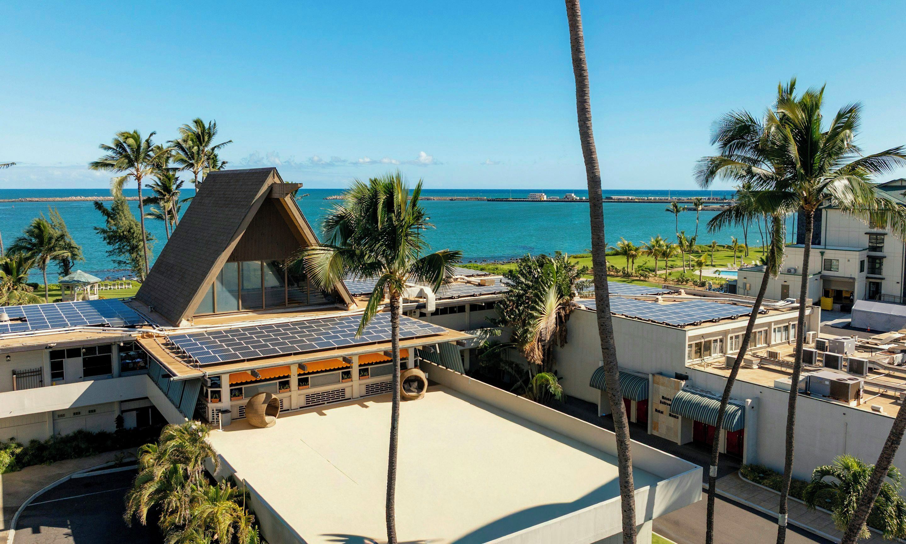 Un resort con piscina en la azotea, paneles solares y vista al océano.