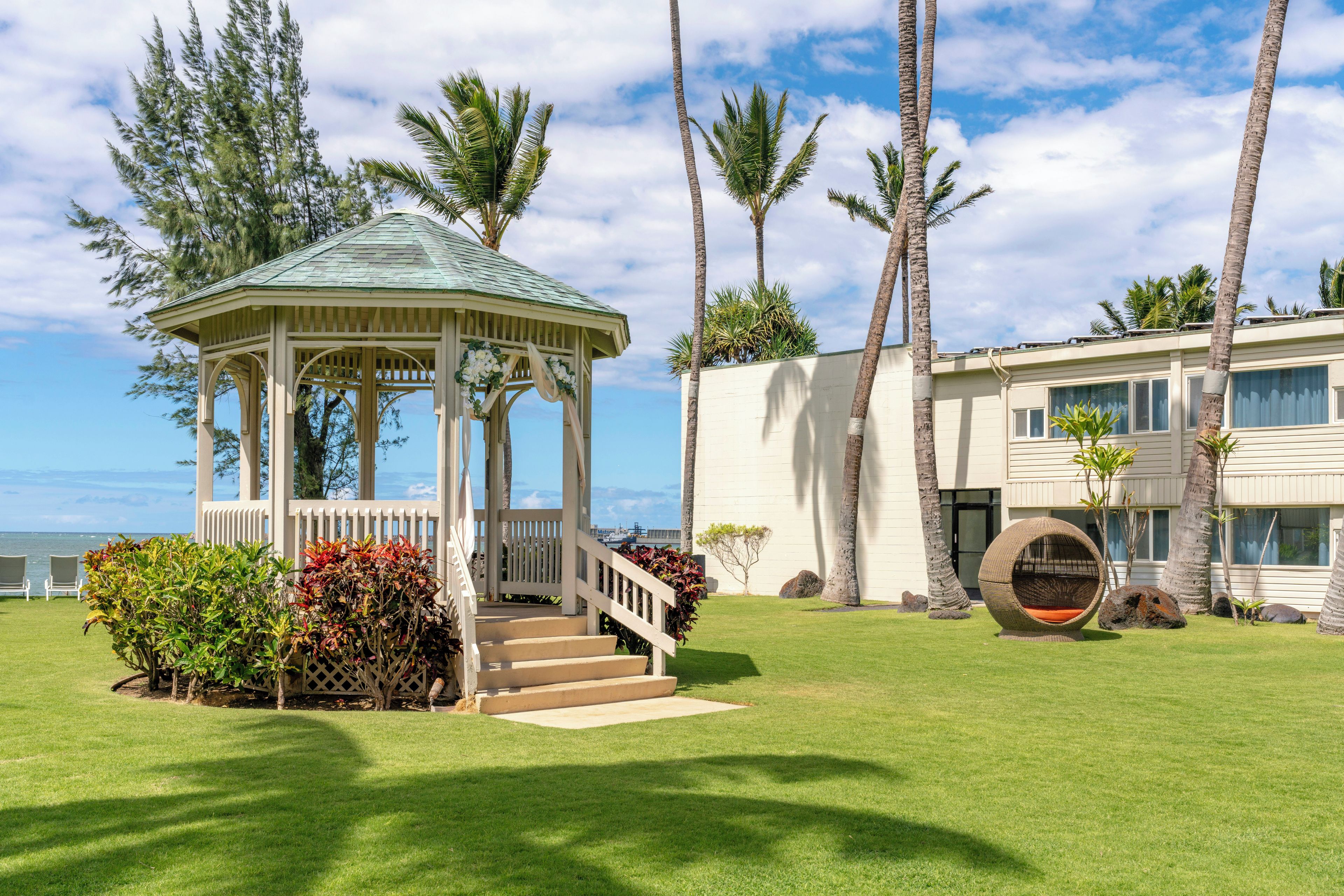 A gazebo with a view of the ocean, a building with a balcony, and palm trees.
