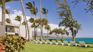 A resort with a poolside area featuring white lounge chairs, palm trees, and a view of the ocean. - Maui Beach Hotel (Kahului)