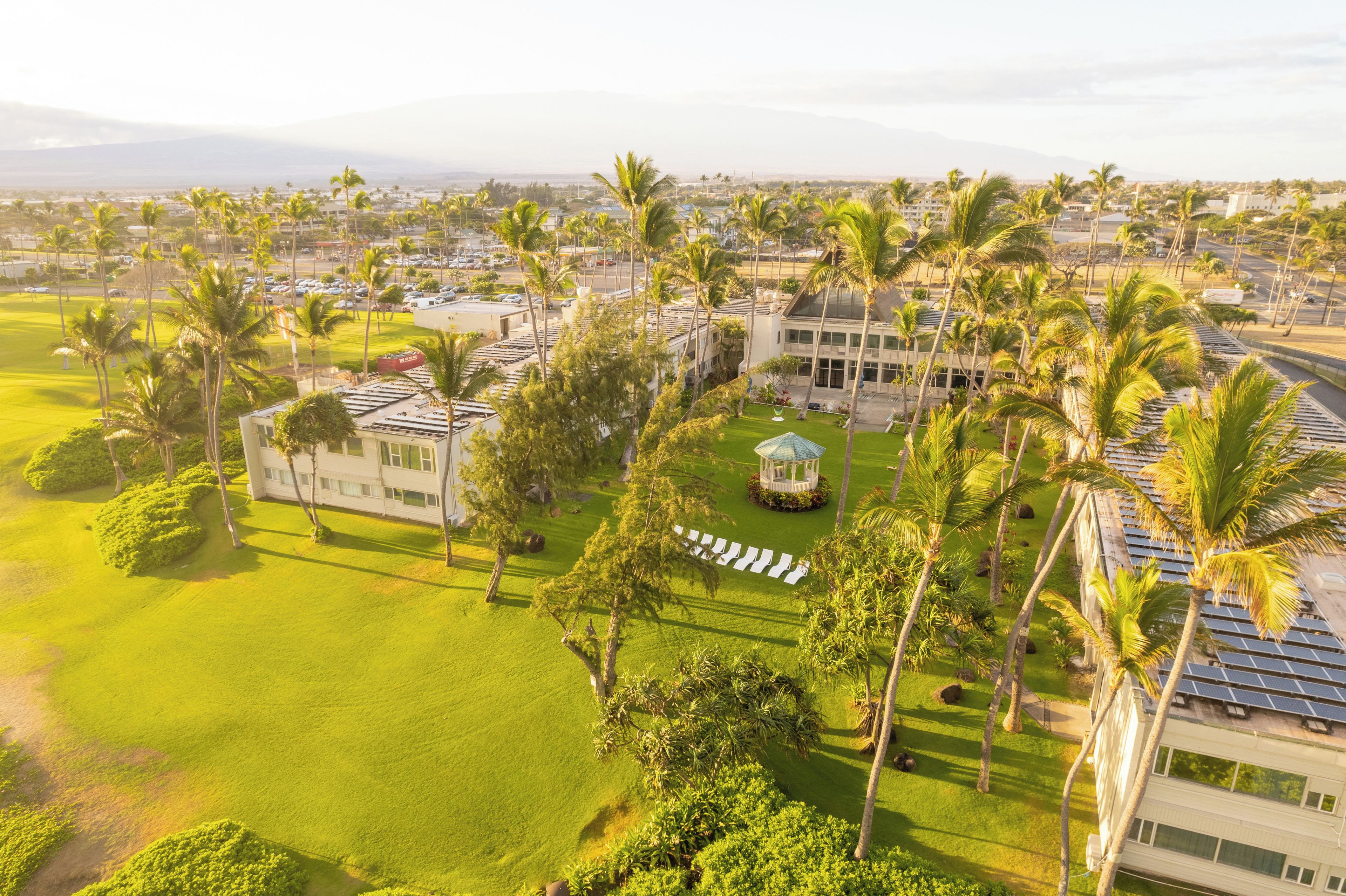 An aerial view of a resort with multiple buildings, palm trees, and a well-maintained lawn.
